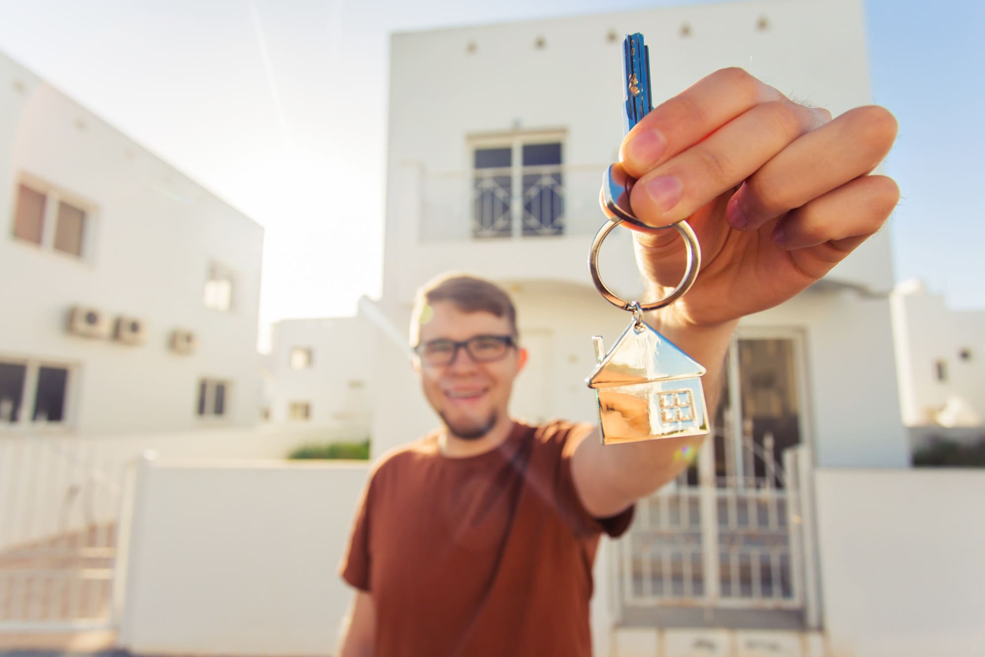 Concept of housewarming, real estate, new home - Young man holding key of new house
